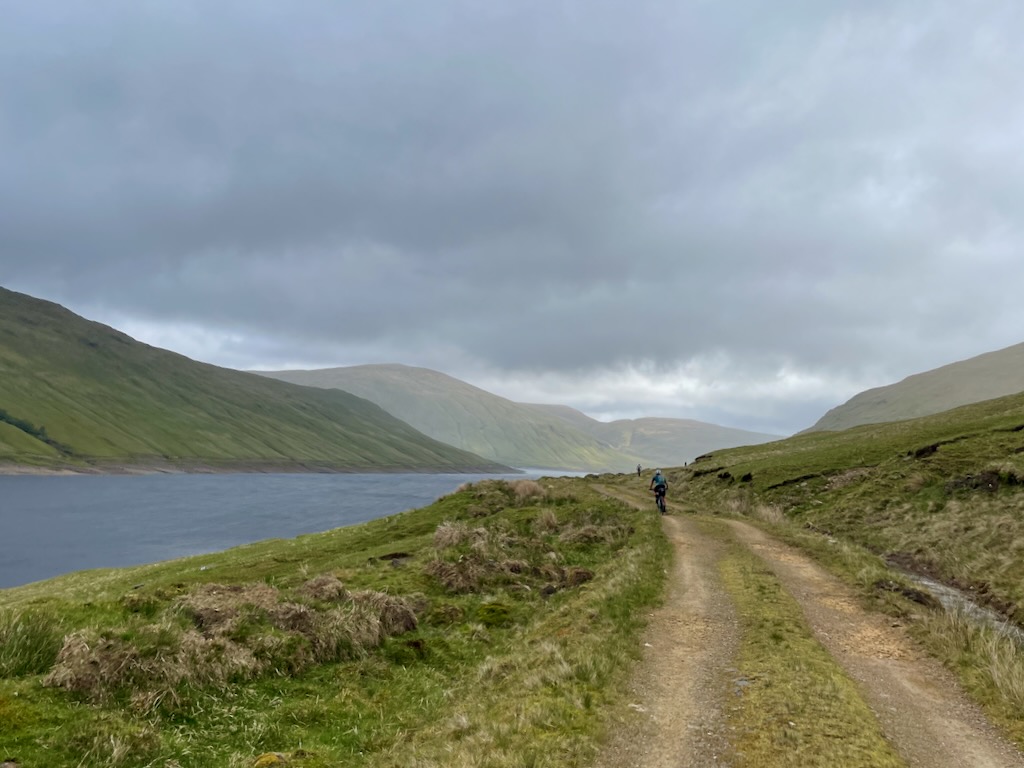 riders along side a loch on a gravelly trail