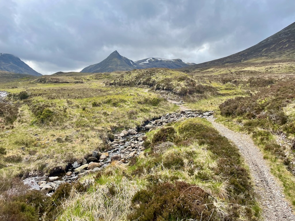 looking up a singletrack descent, with rocky stream and pointed mountain in background